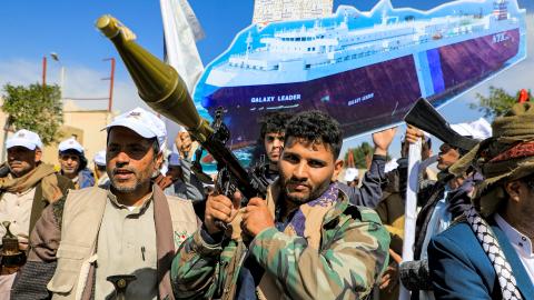 A sign depicting a cutout of the Bahamas-flagged cargo vessel Galaxy Leader, which was seized by fighters of Yemen's Huthi movement in late 2023, is raised by a protester behind a man carrying a rocket-propelled grenade (RPG) launcher during a pro-Palestinian rally in the Huthi-held capital Sanaa on February 7, 2024 amid the ongoing conflict in the Gaza Strip between Israel and the Palestinian militant group Hamas. (Photo by MOHAMMED HUWAIS / AFP) (Photo by MOHAMMED HUWAIS/AFP via Getty Images)