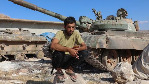 A Syrian rebel fighter checks his phone next to a tank in a rebel training camp near the Bab al-Hawa crossing between Iblib province and Turkey. (Getty Images)