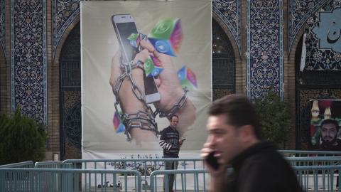 An Iranian man holding his smartphone looks on while standing under an anti-Social networking banner in Tehran Grand Bazaar (Market), December 3, 2022. (Photo by Morteza Nikoubazl/NurPhoto via Getty Images)
