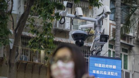 A woman wearing face mask walks in front of a dozen of CCTV Camera on December 29, 2022 in Macau, China. (Photo by Vernon Yuen/NurPhoto via Getty Images)