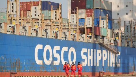 Dockworkers walk past a Cosco Shipping container ship at the Chinese port of Yantai on December 29, 2022. (CFOTO/Future Publishing via Getty Images)