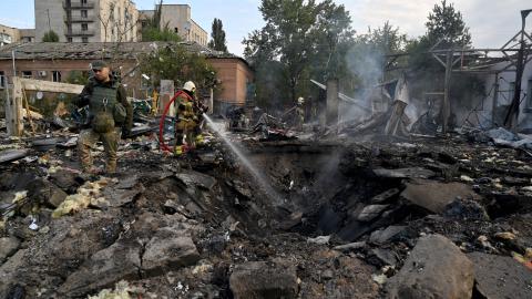 Firefighters push out a fire as police experts look for fragments of missile at a crater on an industrial area of the Ukrainian capital of Kyiv, after a massive overnight missile attack to Ukraine on September 21, 2023. (Sergei Supinkey/AFP via Getty Images)