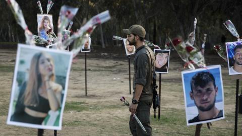 A soldier walks with a rose near photos of people killed during Hamas's attack on the Nova festival at the site on November 29, 2023, in Re'im, Israel. (Photo by Amir Levy/Getty Images)