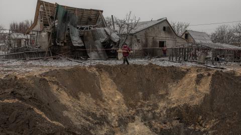 Communal workers walk next to a crater and destroyed houses following a Russian shelling in Kyiv on December 11, 2023. (Roman Pilipey/AFP via Getty Images)