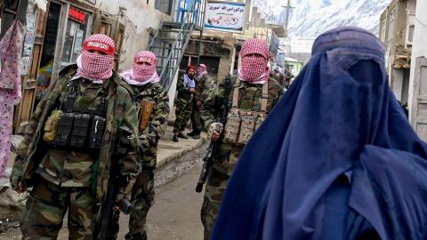 Taliban security personnel stand guard as a burqa-clad woman walks along a street at a market in the Baharak district of Badakhshan province. (Wakil Kohsar/AFP via Getty Images)