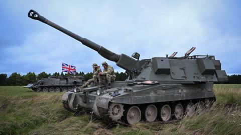 British soldiers sit on a AS90 155mm self-propelled gun as Ukrainian artillery recruits undergo a live fire training exercise, on July 27, 2023 in South West, England. The UK was the first country to donate Western main battle tanks by gifting a squadron of Challenger 2 tanks with armoured recovery and repair vehicles, as well as a battery of eight AS90 guns at “high readiness” and a further two batteries at “varying states of readiness.” The AS90 is an agile, highly accurate, modern artillery system which