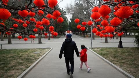 A man and a child walk along a road with red lanterns hanging on trees for the upcoming Chinese Lunar New Year celebrations at a park in Beijing on January 11, 2023. (Wang Zhao/AFP via Getty Images)