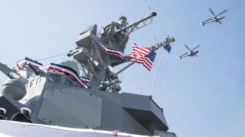 U.S. Navy Sailors with Arleigh Burke-class guided missile destroyer USS John Basilone (DDG 122), climb the brow as U.S. Marine Corps helicopters with Marine Aircraft Group 49, fly over during a commissioning ceremony on Nov. 9, 2024 at New York, New York.