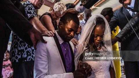 TOPSHOT - Bride and groom Sharon and Mcvivien kneel as elders pray over them following their nuptials mass during their wedding ceremony in Nairobi, Kenya, on February 13, 2016. The couple had their white-wedding in Kibera, famous as the largest slum in Africa, where they grew up and their modern nuptials are representative of a growing middle-class increasingly able and willing to spend more on lifestyles. (Photo by FREDRIK LERNERYD / AFP) (Photo by FREDRIK LERNERYD/AFP via Getty Images)