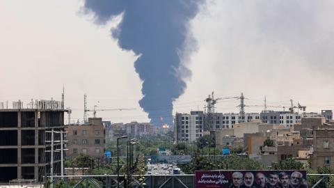 Portraits of Iranian military generals and nuclear scientists killed in Israel’s June 13 attack are displayed above a road as a plume of heavy smoke and fire rise over an oil refinery in southern Tehran on June 15, 2025. (Atta Kenare via Getty Images)
