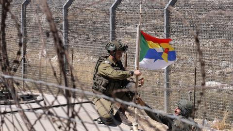 An Israeli soldier attaches a Druze flag to the antenna of a Humvee along a barbed-wire fence in the Golan Heights near the Druze village of Majdal Shams on July 19, 2025. (Jalaa Marey via Getty Images)