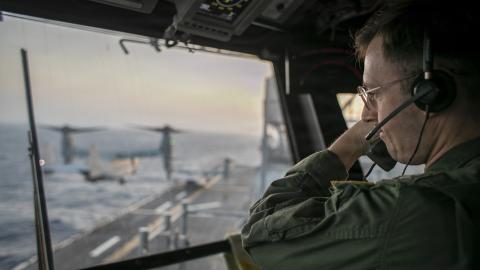 A naval officer aboard USS Tripoli (LHA 7) oversees flight operations from the control tower as the amphibious assault ship sails in the Arabian Sea. U.S. warships and aircraft deployed to the Middle East are enforcing the naval blockade against Iran while executing Project Freedom to support the free flow of commerce through the Strait of Hormuz. (U.S. Navy Photo)