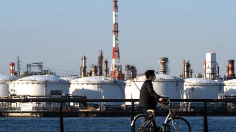 A man pushes his bicycle in front of oil storage tanks at a refinery on March 12, 2026, in Kawasaki, Kanagawa Prefecture, Japan. (Getty Images)