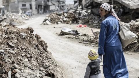 A Kurdish Syrian woman walks with her child past the ruins of the town of Kobane, also known as Ain al-Arab, on March 25, 2015. (YASIN AKGUL/AFP/Getty Images)