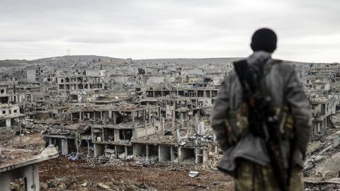 A Kurdish marksman stands atop a building looking at the destroyed Syrian town of Kobane, also known as Ain al-Arab, on January 30, 2015. (BULENT KILIC/AFP/Getty Images)