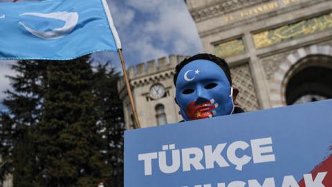 A demonstrator wearing a mask painted with the colors of the flag of East Turkestan holds a placard reading "Speaking Turkish, banned." during a protest by supporters of the Uyghur minority on April 1, 2021, at Beyazid Square in Istanbul.  (Getty Images)