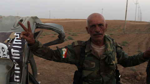 A Peshmerga fighter next to the remains of a car bearing the Islamic State's trademark jihadist flag after an American air strike in the village of Baqufa, north of Mosul, on August 18, 2014. (AHMAD AL-RUBAYE/AFP/Getty Images)