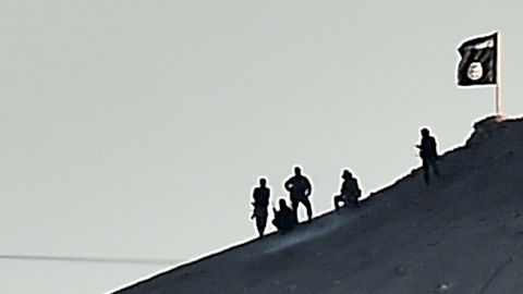 Alleged Islamic State (IS) militants stand next to an IS flag atop a hill in the Syrian town of Ain al-Arab, on October 6, 2014. (ARIS MESSINIS/AFP/Getty Images)