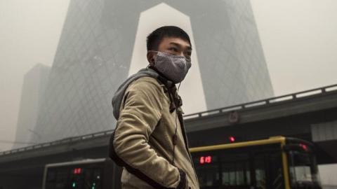 A Chinese man wears a mask as he waits to cross the road near the CCTV building during heavy smog on November 29, 2014 in Beijing, China. (Kevin Frayer/Getty Images)