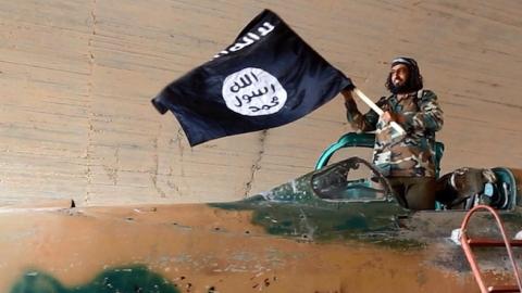 Islamic State fighter waving a flag while standing on a captured government fighter jet in Raqqa, Syria, 2015. (Universal History Archive/UIG via Getty Images)