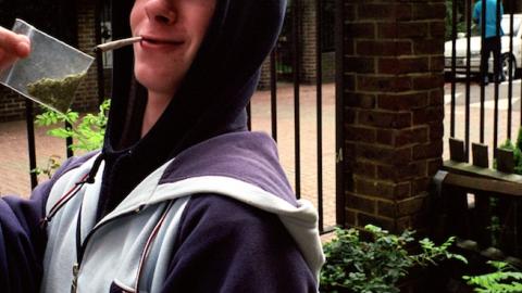 Stoned teenage boy smoking spliff and triumphantly holding a bag of weed, Lambeth Walk South London c.2000. (PYMCA/UIG via Getty Images)