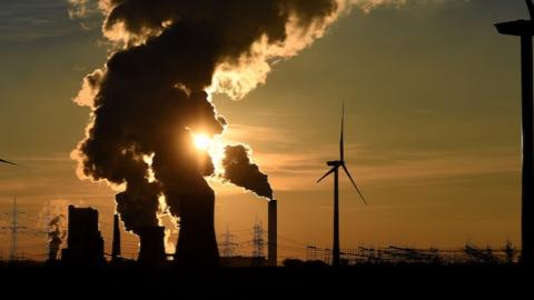 Electricity pylons and wind turbines stand beside a coal-fired power plant while steam rises from cooling towers near Bergheim, Germany (Photo by Volker Hartmann/Getty Images)