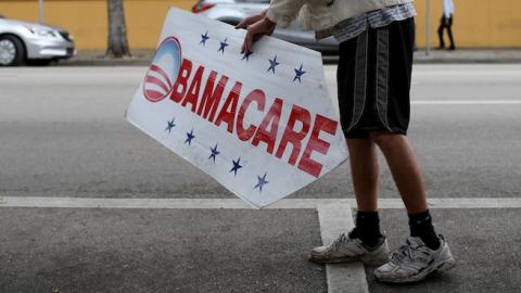 A man holds up a sign directing people to an insurance company where they can sign up for the Affordable Care Act (Photo by Joe Raedle/Getty Images)