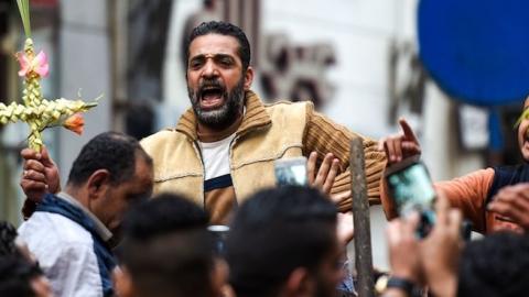 An Egyptian raises a cross made of palm leaves, originally intended for Palm Sunday celebrations, as he is being lifted by others at the Coptic Orthodox Patriarchate in Alexandria, April 9, 2017. (MOHAMED EL-SHAHED/AFP/Getty Images)