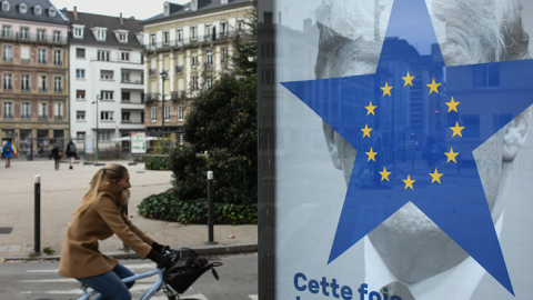 A cyclist rides near a street poster depicting the twelve-star circle from the European Union flag within a blue five-pointed star covering the face of what is deemed to be a portrait of US President Donald Trump. (SEBASTIEN BOZON/Getty Images)