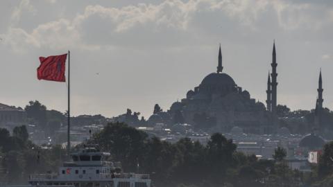 A ferry navigates the Bosphorus Strait in front of a Turkish flag and the Suleymaniye Mosque in Istanbul, Turkey. (Getty Images)