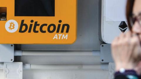 A woman uses her phone as she walks past an ATM for the digital currency bitcoin in Hong Kong on Dec. 18, 2017