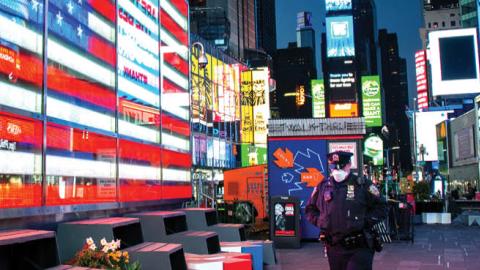 An NYPD officer wearing a protective mask walks past an American Flag in an empty Times Square at night amid the coronavirus pandemic on April 22, 2020 in New York City.