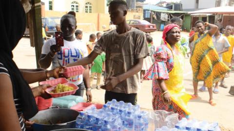 A food vendor serving food as people queue in line to collect food as Lagos state government begins distribution of meals to Youths in verious LCDAs, Local Community Development Areas as part of measures to prevent the spread of COVID-19 in Lagos, on Apri