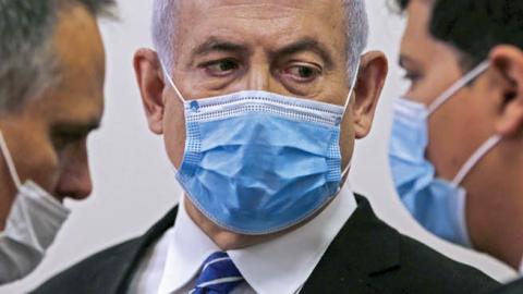 Israeli Prime Minister Benjamin Netanyahu (C), wearing a protective face maks, speaks with his lawyer inside a courtroom at the district court of Jerusalem on May 24, 2020, during the first day of his corruption trial.