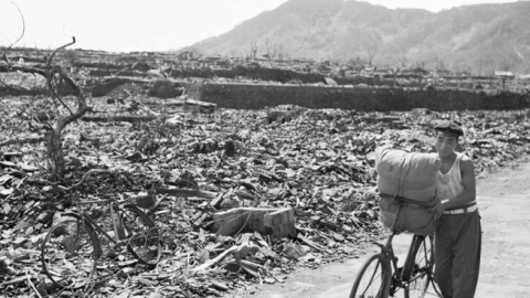 09/13/1945-A Japanese civilian pushes his loaded bike down a path which has been cleared of rubble. On either side of the path debris, twisted metal, and gnarled tree stumps fill the area. (Getty Images)