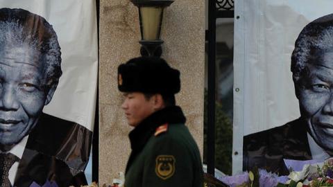 A Chinese policeman walks past a memorial to the late South African leader Nelson Mandela outside the South African embassy in Beijing on December 11, 2013. 