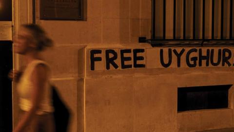 A woman walks past a banner pasted by members of a collective against violence towards women in support of the Uighur population on a wall of China's Embassy in Paris on July 30, 2020.