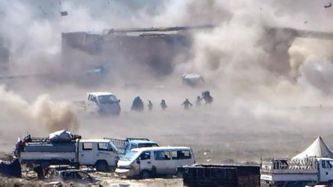 People are seen fleeing as heavy smoke rises above the Islamic State (IS) group's last remaining position in the village of Baghouz during battles with the Syrian Democratic Forces (SDF)