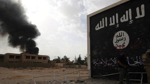 Iraqi fighters of the Hashed al-Shaabi stand next to a wall bearing the Islamic State group flag as they enter the city of al-Qaim, in Iraq's western Anbar province near the Syrian border (AHMAD AL-RUBAYE/AFP via Getty Images)