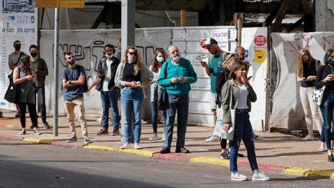 People wait for the bus on a street in the Israeli coastal city of Tel Aviv on April 18, 2021 (Photo by JACK GUEZ/AFP via Getty Images)