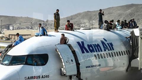 Afghan people climb atop a plane as they wait at the airport in Kabul on August 16, 2021 (Photo by WAKIL KOHSAR/AFP via Getty Images)