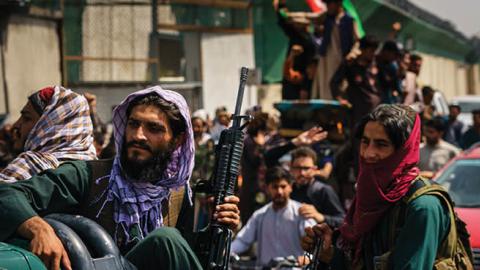 Afghans march down the street carrying banners and the flag of the Islamic Republic of Afghanistan, despite the presence of Taliban fighters around them, in Kabul, Afghanistan, Thursday, Aug. 19, 2021 (MARCUS YAM / LOS ANGELES TIMES)
