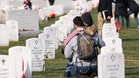Army veteran Stephen Hedger is hugged by his son Lincoln as he visits the gravesite of U.S. Army Major Paul Douglas Carron at Arlington National Cemetery on Veterans Day, November 11, 2021 in Arlington, Virginia. (Photo by Anna Moneymaker/Getty Images)