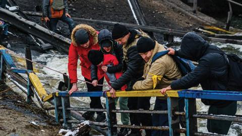 Soldiers help civilians cross a broken bridge as they flee their besieged city of Irpin, Ukraine, Tuesday, March 1, 2022. (Marcus Yam/Los Angeles Times/Getty Images)