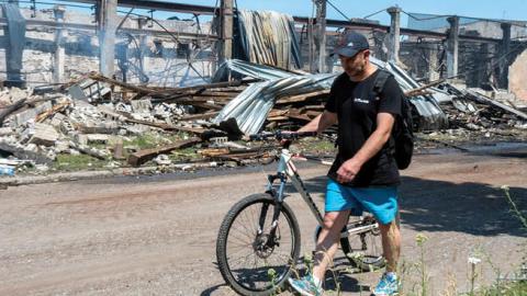 A man pushes a bicycle as he walks past a building of Mashgidroprivod plant, which was destroyed by a Russian missile attack in Kharkiv on June 29, 2022, amid the Russian invasion of Ukraine. (Photo by Sergey Bobok/AFP via Getty Images)