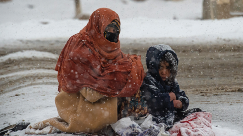 An Afghan woman begs for money from passing cars in the snow, with her child huddled beside her, on the Kabul road south to Pul-e Alam, Afghanistan, on January 17, 2022. (Scott Peterson/Getty Images)