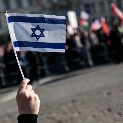 BERLIN, GERMANY - 2025/09/27: A protester holds an Israeli Flag during the counter demonstration. Tens of thousands of people marched in Berlin under the slogans "All Eyes on Gaza" and "Stop the Genocide," demanding a ceasefire, peace talks, and an end to German arms exports to Israel. Protesters carried Palestinian flags and banners, while police deployed 1,800 officers to maintain order. Organizers accused the German government of supporting Israel's actions in Gaza, which they descr