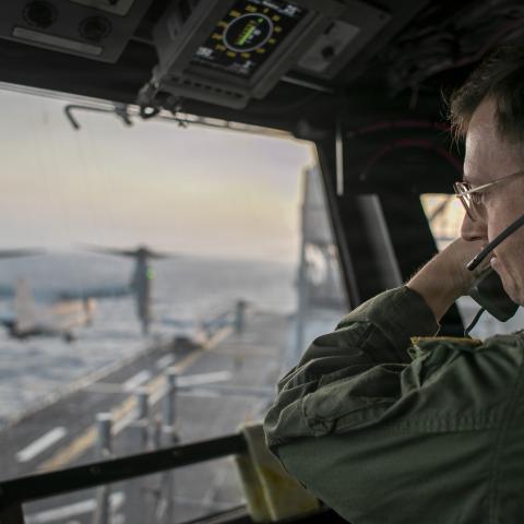 A naval officer aboard USS Tripoli (LHA 7) oversees flight operations from the control tower as the amphibious assault ship sails in the Arabian Sea. U.S. warships and aircraft deployed to the Middle East are enforcing the naval blockade against Iran while executing Project Freedom to support the free flow of commerce through the Strait of Hormuz. (U.S. Navy Photo)
