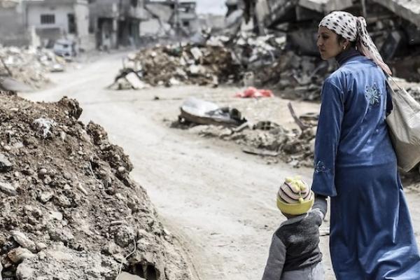 A Kurdish Syrian woman walks with her child past the ruins of the town of Kobane, also known as Ain al-Arab, on March 25, 2015. (YASIN AKGUL/AFP/Getty Images)