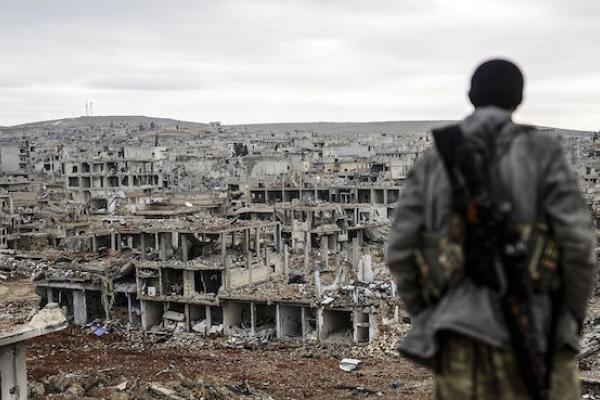 A Kurdish marksman stands atop a building looking at the destroyed Syrian town of Kobane, also known as Ain al-Arab, on January 30, 2015. (BULENT KILIC/AFP/Getty Images)